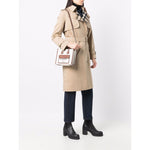 Person holding Burberry mini tote bag with cream/brown color, logo print, and gold-tone hardware, styled with trench coat and boots.