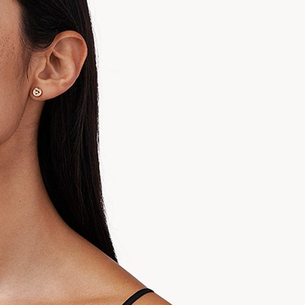 Close-up of a woman's ear wearing a small gold heart-shaped earring.