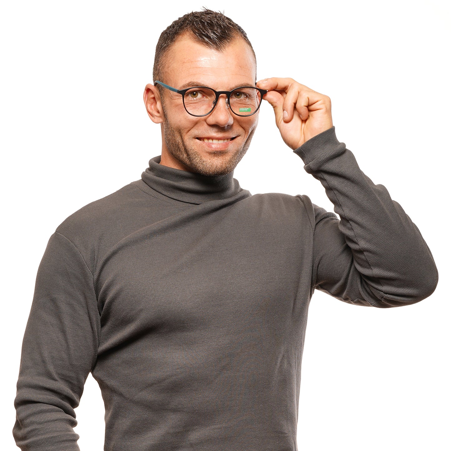 Man wearing Benetton MOD. BEO1010 51001 glasses, smiling and adjusting eyewear, dressed in a gray turtleneck shirt.
