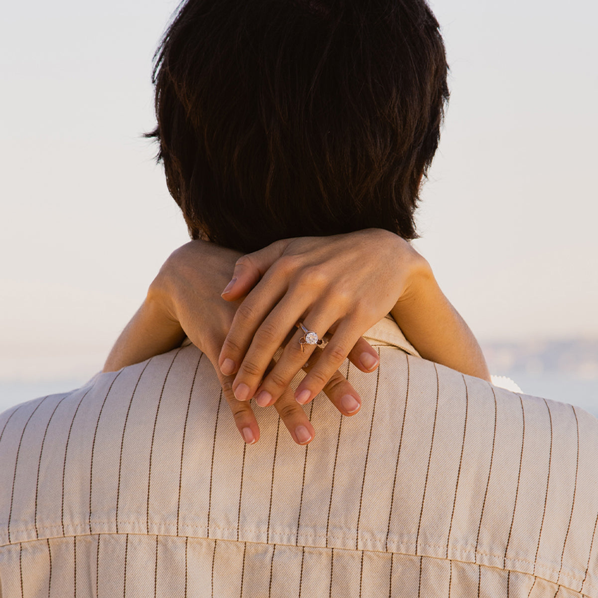 Elegant embrace showcasing a diamond ring on hands around a partner.