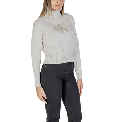 Woman wearing Calvin Klein Jeans Cream Cotton Turtleneck with CK logo, featuring a ribbed turtleneck and cropped fit for modern style.