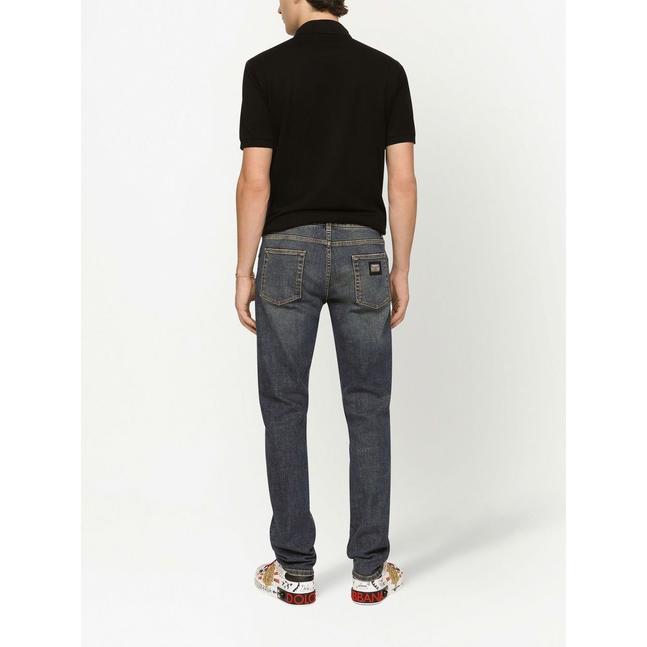 Back view of a man wearing a black Dolce & Gabbana Logo cotton polo shirt with jeans and patterned sneakers.