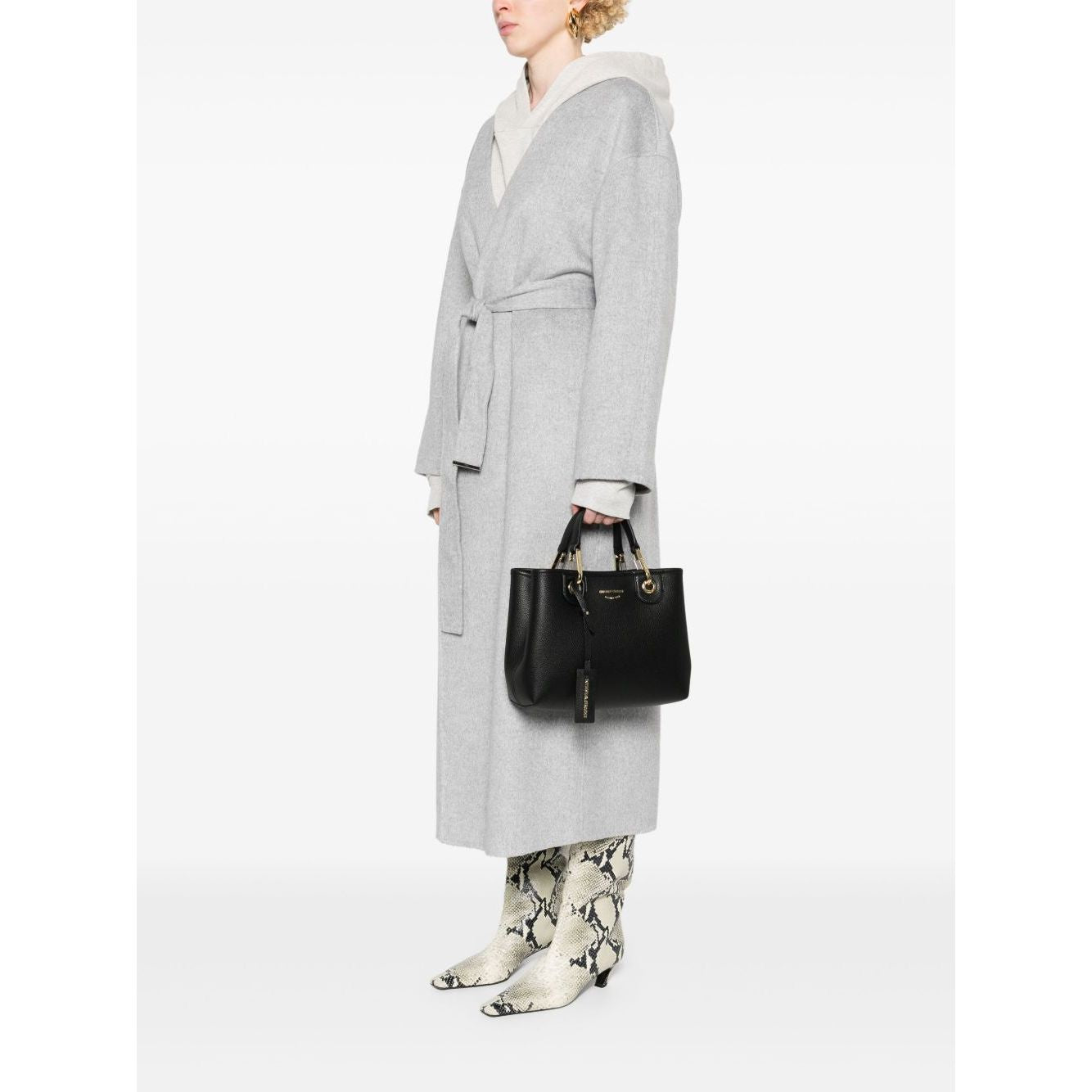 Person holding Emporio Armani MyEA small shopping bag in black faux leather with grained texture and gold-tone hardware, wearing grey coat.