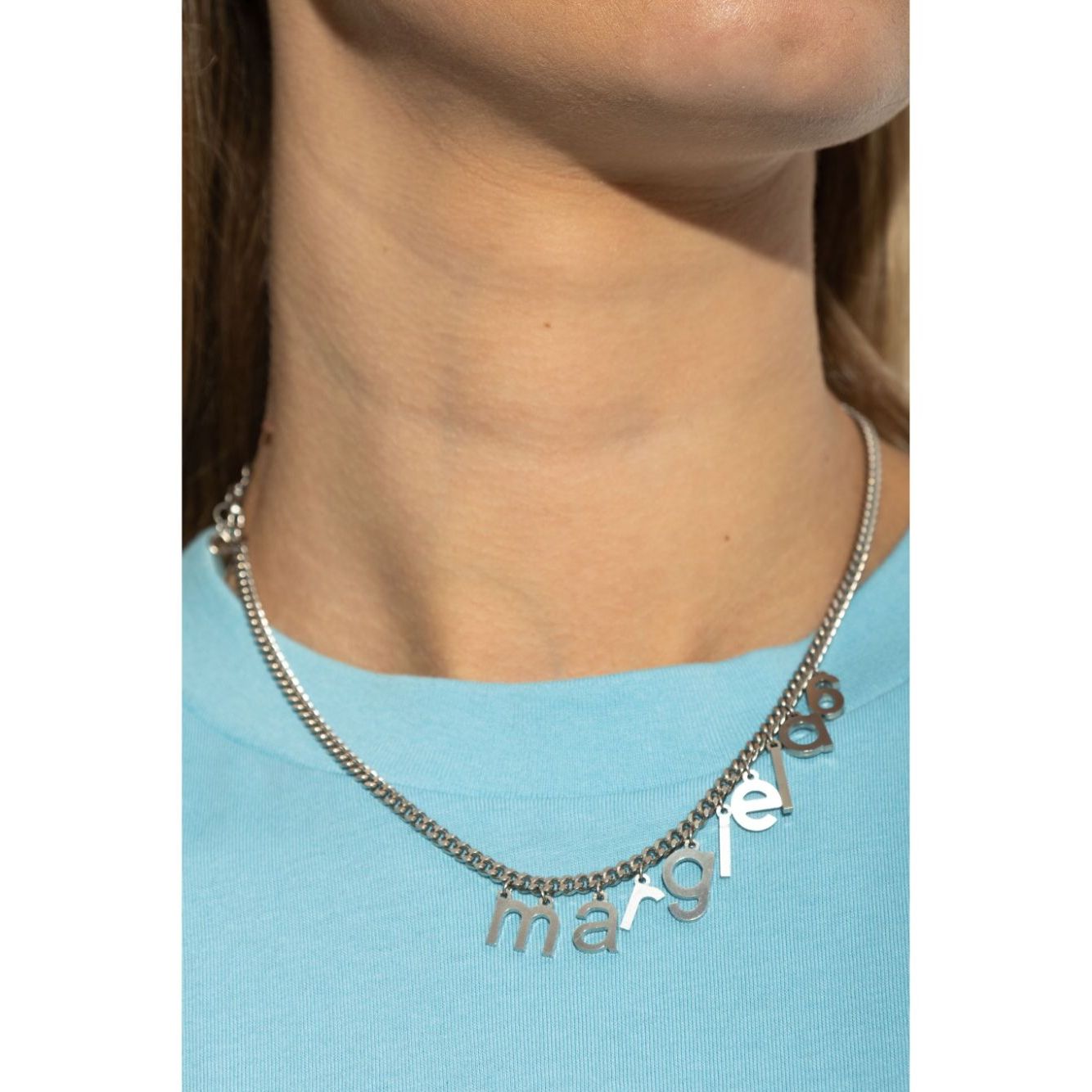 Close-up of MM6 Maison Margiela logo-lettering necklace with silver-tone curb chain and adjustable fit on a person wearing a blue shirt.