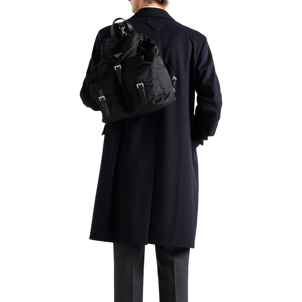 Back view of a model wearing Prada Blue Wool Coat, showcasing the straight hem and back triangle logo detail, with a black backpack.